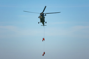 Rescue helicopter and rescuer on the rope - life-saving flying vehicle and blue sky (muted contrast)