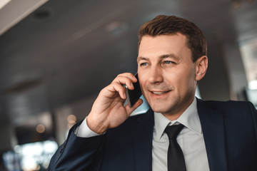 Interested businessman speaking on smartphone and looking ahead with smile