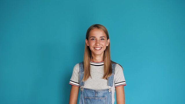 Happy smiling caucasian young girl. Portrait of cute teen girl with long hair smiling at the camera on blue background. Close up, portrait of attractive girl smiling confident and pretty
