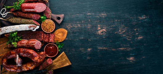 Assortment of salami and snacks. Sausage Fouet, sausages, salami, paperoni. On a black wooden background. Top view. Free space for your text.