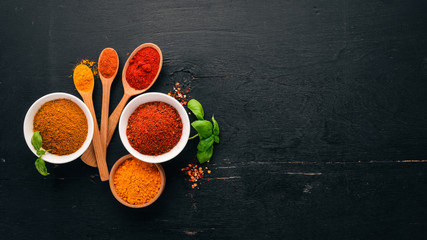 Spices and herbs on a wooden board. Pepper, salt, paprika, basil, turmeric. On a black wooden chalkboard. Top view. Free copy space.