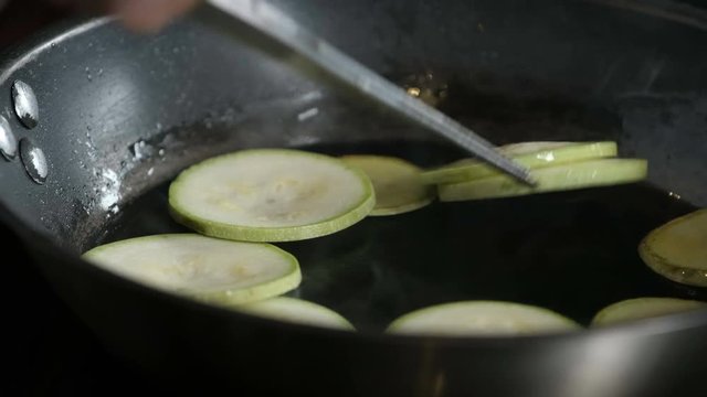the chef gently turns the zucchini in a frying pan. tweezers