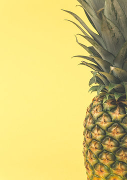 A close up of the patterned outer skin of a fresh pineapple showing its leaves with copy space and yellow background.