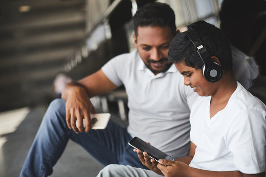 Joyful delighted little boy wearing headset while testing his modern smartphone with his father