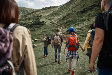 Focus on three ladies and man carrying rucksacks during their ascent on peak. One more couple is...
