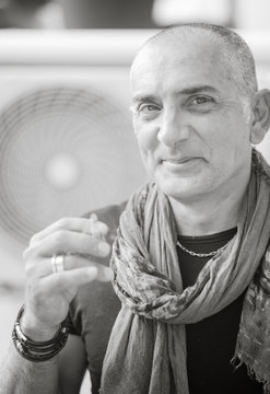 A 50y man is smoking a cigarette. Black and white. The fan coil of an air-conditioner is on the background.