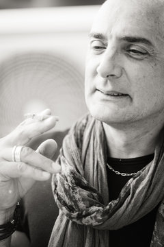 A 50y man is smoking a cigarette. Black and white. The fan coil of an air-conditioner is on the background.
