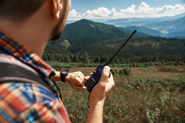Focus on male hand with trekker. Guy standing in highland valley and checking time. He is holding walkie-talkie for communication in extreme conditions