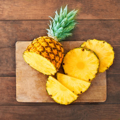 Fototapeta na wymiar Pineapple on wood texture background. Whole and sliced tropical pineapple on wooden cutting board with copy space. Top view.