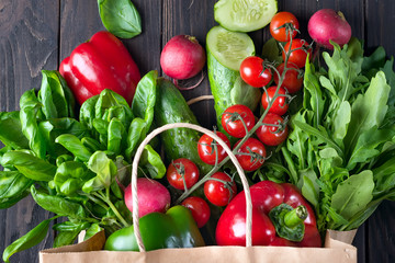 Ingredients for making healthy salad in a paper bag - pepper, cherry tomatoes, cucumber, arugula, basil, radishes, zucchini. Flat lay