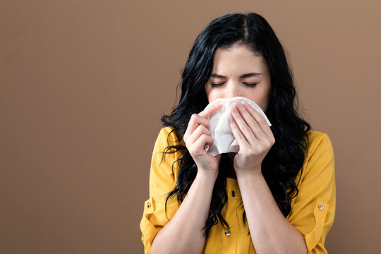 Sick young woman with tissues on a brown background