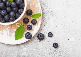 Fresh raw organic blueberries with leaf in white china bowl on stone kitchen background. Space for text