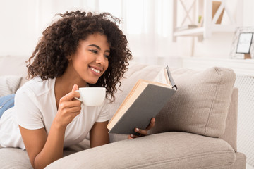 Happy woman drinking tea and reading book on couch