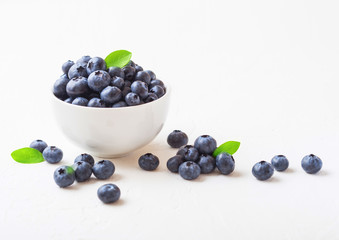 Fresh raw organic blueberries with leaf in white china bowl on white background. Macro close up