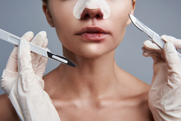 Young woman having bloody lips and two scalpels near her face