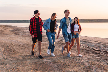 Group of hipster young friends on beach together walking during sunset. Freedom and friendship concept