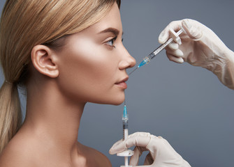 Injection in lips. Calm young pretty lady looking attentively at the professional doctor while getting necessary injections into her lips