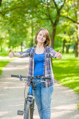 Fototapeta na wymiar Happy young beautiful woman with bike showing thumbs up