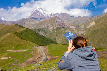 girl looking in binoscope directed towards the snowy mountain tops of Kazbeg from the view point Gergeti Trinity Church Tsminda Sameba Holy Church near the village of Gergeti in Georgia.