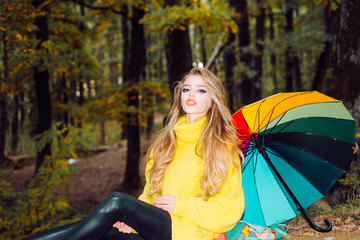 Beautiful Woman with Autumn Leaves on Fall Nature Background. Dreamy girl with long hair in knit sweater. Autumn portrait woman holds yellow maple leaves in park. Female autumn fashion concept.