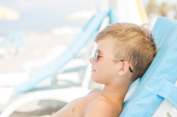the boy on a sunny beach lies on a sun lounger in sunglasses