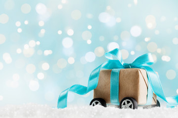 Christmas gift or present box on wheels against turquoise bokeh background. Holiday greeting card.