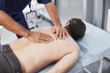 Male patient lying on couch while medical advisor making special therapeutic back massage