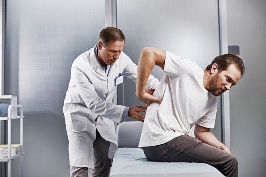 Medical adviser carefully inspecting back of young man and looking for center of pain