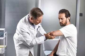 Obraz premium Waist up portrait of doctor testing flexion of elbow joint of patient and testing for any discomfort