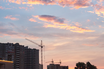 Sunset in city. Crane is building multi-storey house