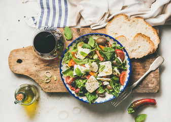 Flat-lay of traditional Greek salad with feta cheese, olive oil in bottle and olives and glass of...