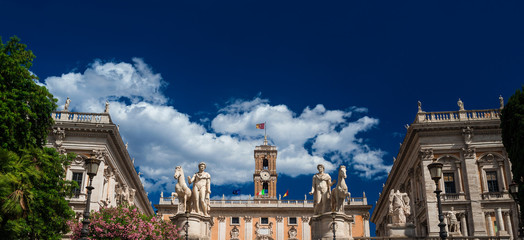 Capitoline Hill with ancient roman statues and renaissance clocktower with clouds, in the very...