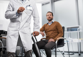 Smiling male patient locating n chair and listening attentively to doctor. Medical adviser explaining various treatments