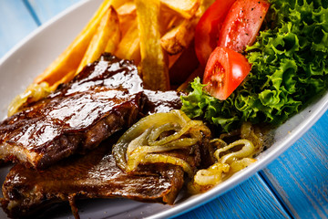 Grilled ribs, French fries and vegetables on wooden background