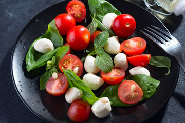 Tasty and beautiful Caprese salad on the black ceramic plate, close up
