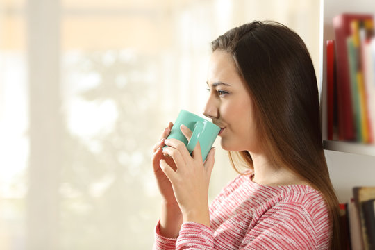 Relaxed woman drinking coffee leaning on shelves