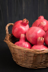 Ripe red pomegranates in wicker basket closeup photography on black background.