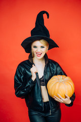 Emotional young women in halloween costumes on party over red background with pumpkin. Witch posing with Pumpkin.