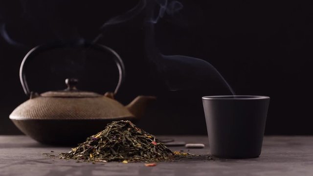 un tas de feuilles de th&eacute; avec une tasse noire et une th&eacute;i&egrave;re en fond