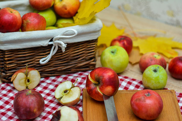 Naklejka na ściany i meble Whole and sliced apples on a red and white checkered cloth, a knife, a basket of apples.