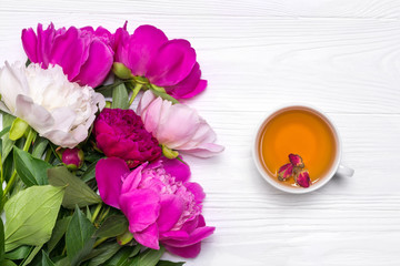 A cup of tea and peonies flowers on a white wooden background. Mockup for your design. View from above.