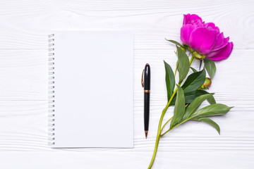 Naklejka premium Empty notepad with place for text, pen and peony flower on a white wooden background. Mockup for your design. View from above.