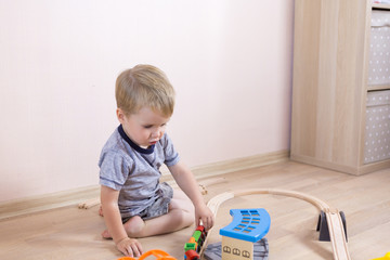 Cute kid boy playing with toy railway road at home at floor, independent children's games
