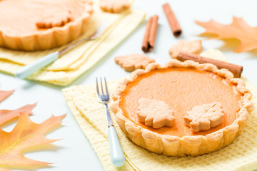 Pumpkin pie with cinnamon and cookies on yellow napkins on pastel blue background with autumn yellow leaves.