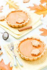 Pumpkin pie with cinnamon and cookies on yellow napkins on pastel blue background with autumn yellow leaves.