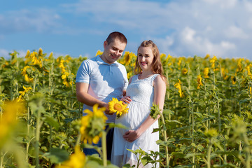 husband and his pregnant wife are walking at sunset in a sunflower field on the outside
