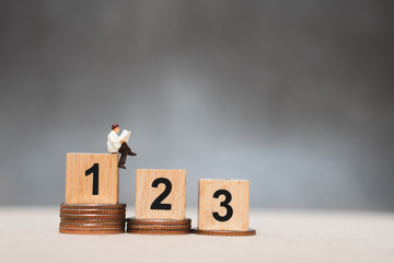 Miniature people, businessman reading on podium and stack coins using as business competition and...