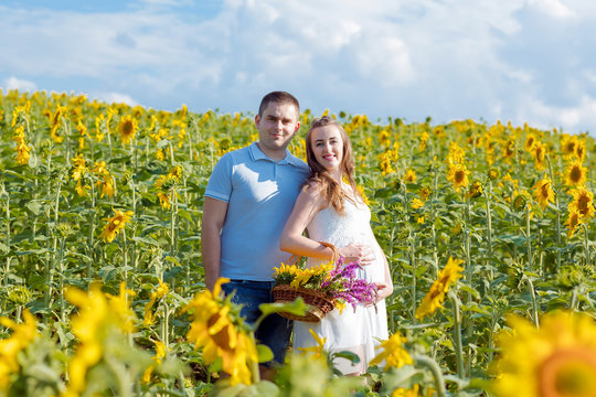 Outdoor portrait of young pregnant couple in sunflowers field on a bright Sunny day. Authentic lifestyle image