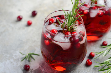 Cold refreshing drink with cranberries and rosemary on a gray concrete background