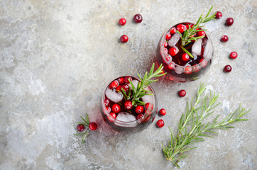 Cold refreshing drink with cranberries and rosemary on a gray concrete background